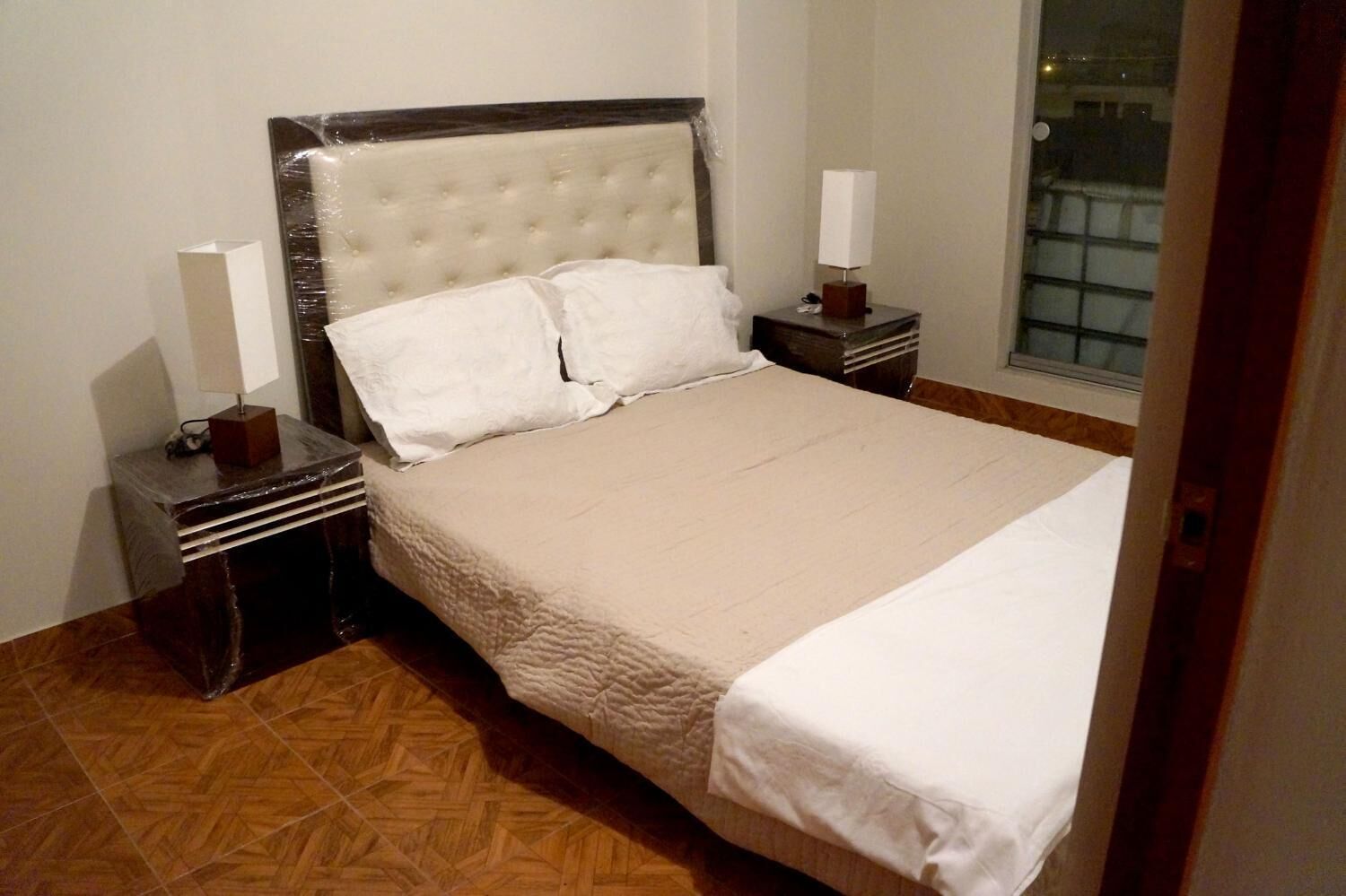 A neatly made bed with a tufted headboard, two bedside tables with lamps, and a herringbone-patterned wooden floor.