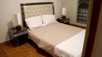 A neatly made bed with a tufted headboard, two bedside tables with lamps, and a herringbone-patterned wooden floor.