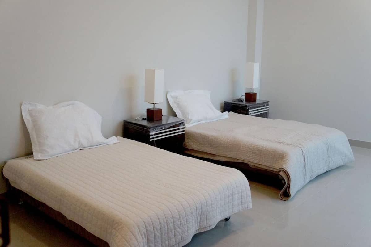 Two single beds with white linens and wooden headboards, each with a bedside table and a lamp.