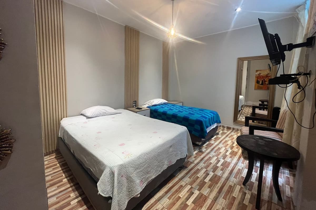 A bedroom with two beds, a TV mounted on the wall, and a small table.