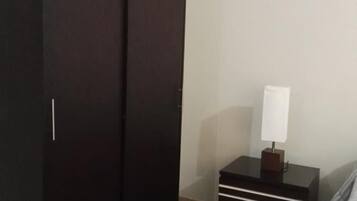 Ein Schlafzimmer mit großem Kleiderschrank, Nachttisch mit Lampe und einem Bett mit gestreifter Bettwäsche.