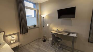 Una habitación de hotel pequeña y ordenada con cama, escritorio, silla y televisor montado en la pared.