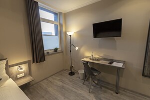 Una habitación de hotel pequeña y ordenada con cama, escritorio, silla y televisor montado en la pared.