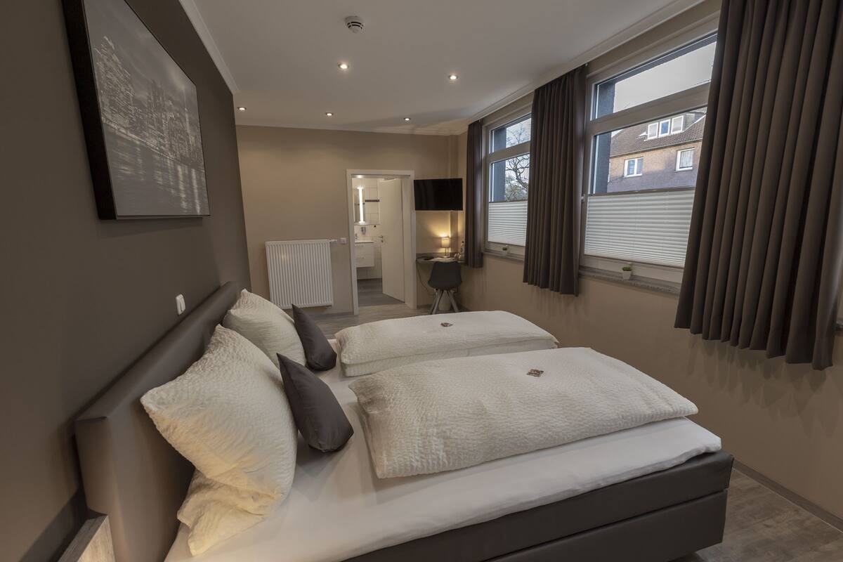 A modern bedroom with a large bed, a walk-in closet, and a view of the city through the window.