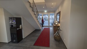 A modern hotel lobby with a red carpet, a staircase, and a reception desk.