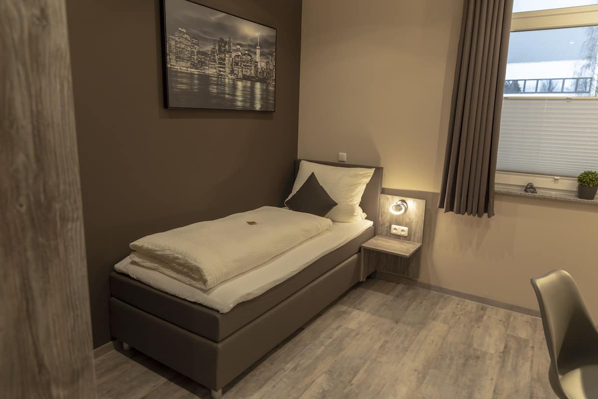 A modern bedroom with a bed, bedside table, and a cityscape painting.