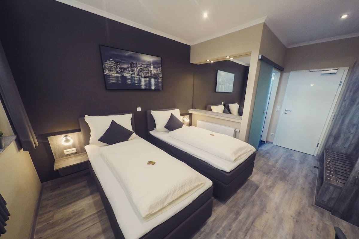 A hotel room with two beds, a cityscape painting, a mirror, and a door.