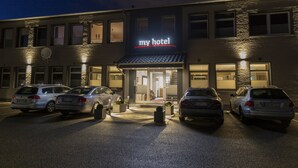 A hotel with a modern facade, a clearly marked entrance, and a parking lot with several cars.