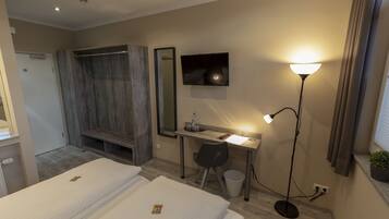 A hotel room with two beds, a desk with a computer, a mirror, a TV, a lamp, and a small plant.