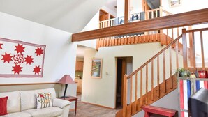 A spacious living area with a high ceiling, a wooden staircase, and a view of the kitchen. - Garden Home: Private Home Downtown Durango (Durango)