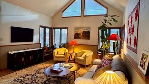 A spacious living room with a high ceiling, large windows, a flat-screen TV, a sofa, two armchairs, a coffee table, and a lamp. - Garden Home: Private Home Downtown Durango (Durango)