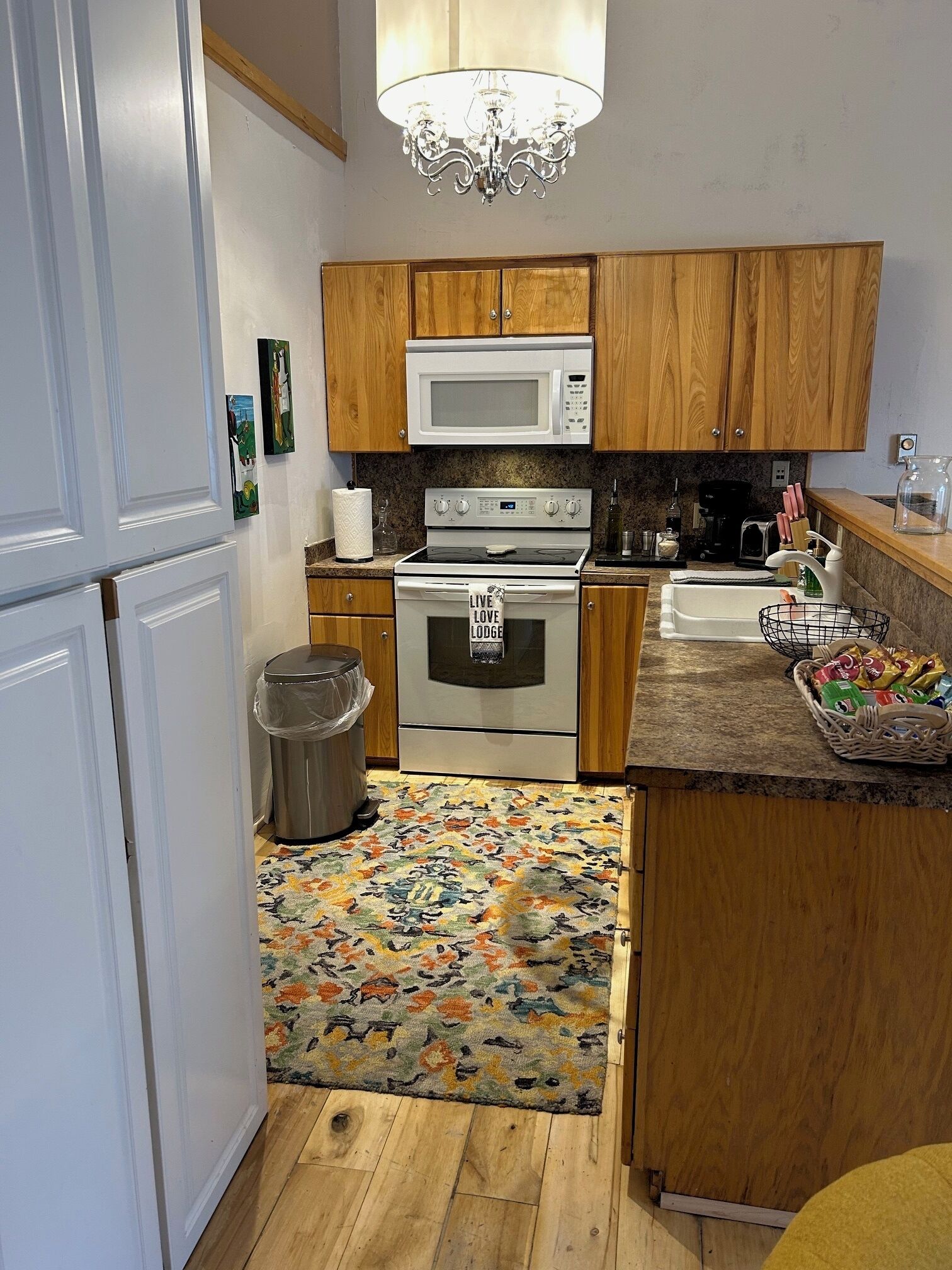 A kitchen with wooden cabinets, a white microwave, an oven, a sink, and a chandelier.