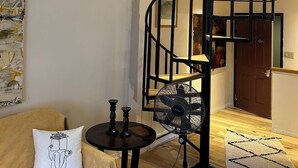 Uma sala de estar com escada em espiral, um ventilador, uma mesinha e um sofá.