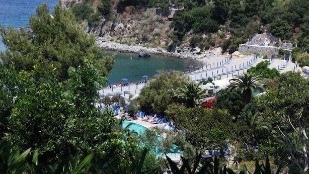 En semesterort vid kusten med en swimmingpool, en strand och klippiga branter.