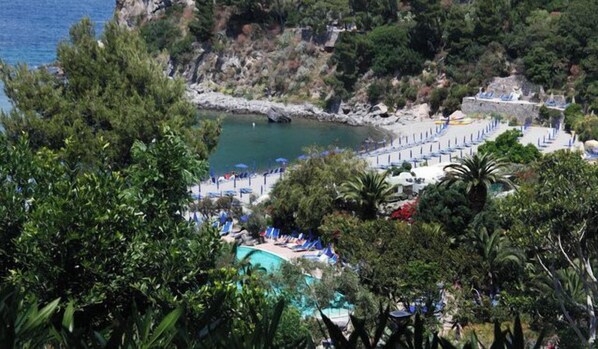 A coastal resort with a swimming pool, beach, and rocky cliffs.