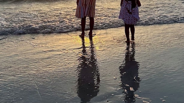 Atardecer sobre el océano con dos personas de pie en la playa.
