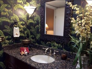 Une salle de bain avec un comptoir en granit, un lavabo blanc et un mur foncé orné d’un motif de feuilles.
