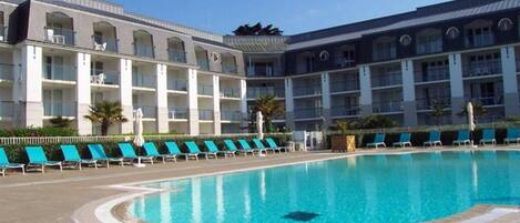 A hotel with a swimming pool surrounded by lounge chairs.