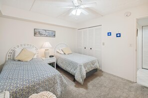 A bedroom with two single beds, a ceiling fan, a nightstand with a lamp, and a painting on the wall.