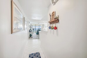 Um corredor com quadros enquadrados, um tapete azul estampado e uma prateleira de madeira com objetos decorativos.