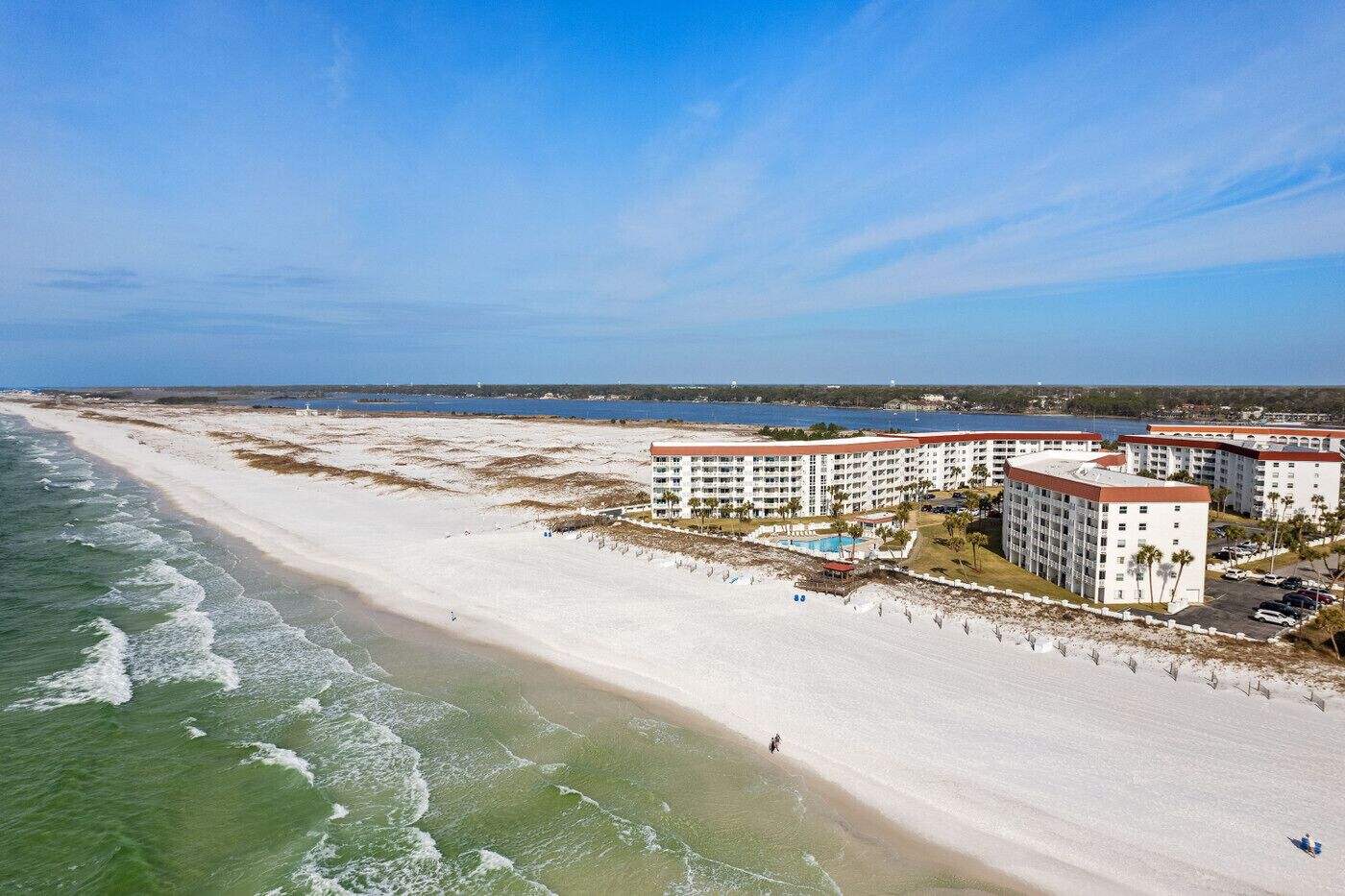 A beachfront hotel with multiple buildings, a sandy beach, and a clear blue sky.