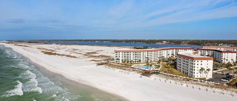 A beachfront hotel with multiple buildings, a sandy beach, and a clear blue sky.