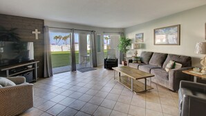 A living room with a TV, sofa, coffee table, and a view of the outdoors.