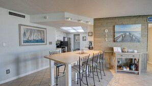 A modern kitchen with a central island, a dining area with chairs, and a wooden wall with a painting.