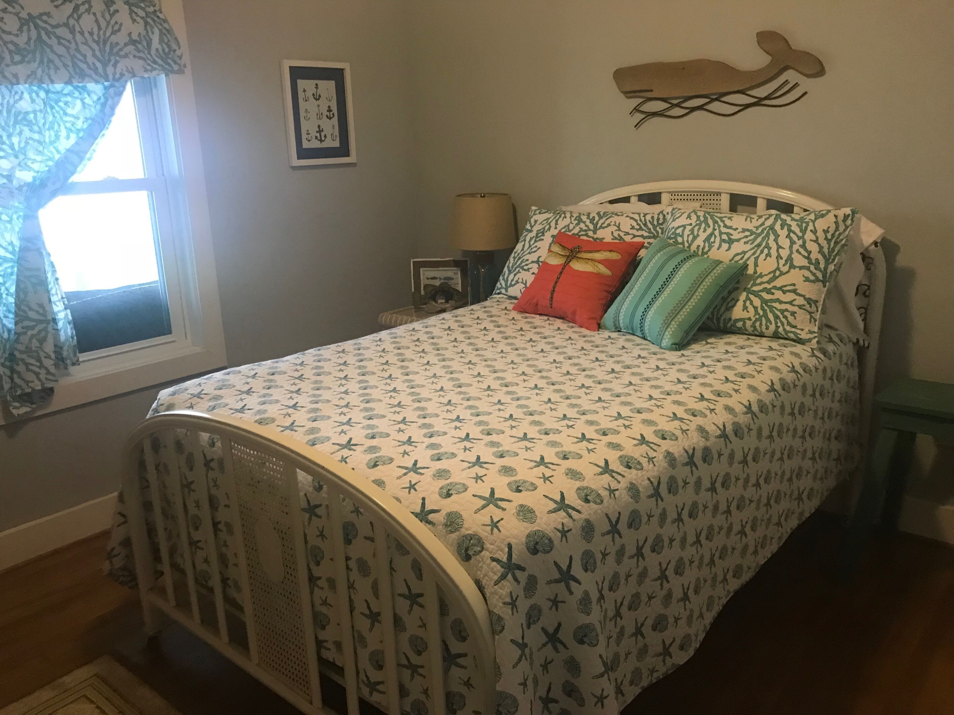 A bedroom with a bed, a window with curtains, a wall-mounted shelf with a lamp, and a framed picture.