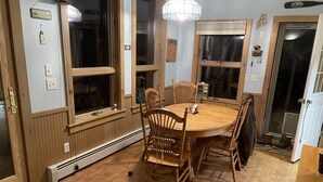 A dining area with a wooden table and chairs, large windows, and a door with a coat rack.