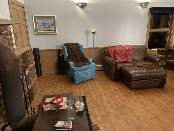 Un salon avec un fauteuil bleu, un canapé en cuir marron, une cheminée et un tableau encadré au mur.