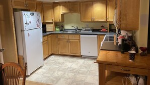 A kitchen with wooden cabinets, a white refrigerator, a dishwasher, and a dining table with chairs.