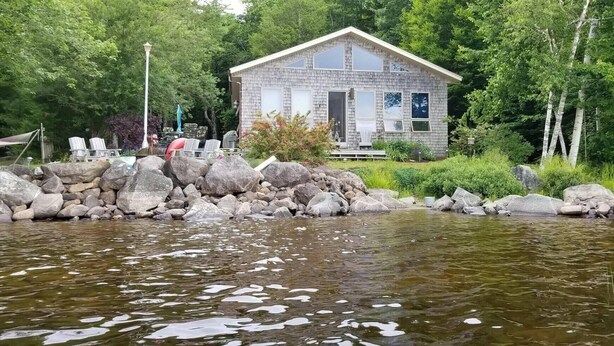 A cabin by a lake with a stone wall and a wooden deck.