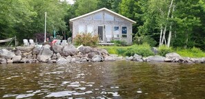 Une cabane au bord d’un lac, avec un mur en pierre et une terrasse en bois.