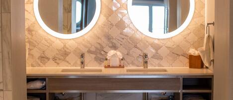 A bathroom with two round mirrors, a marble-patterned wall, and a wooden vanity with towels.