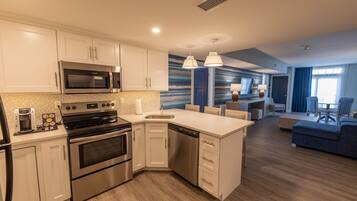 A modern kitchen with stainless steel appliances, a built-in oven, and a dishwasher. There is a dining area with a blue sofa and a lamp.
