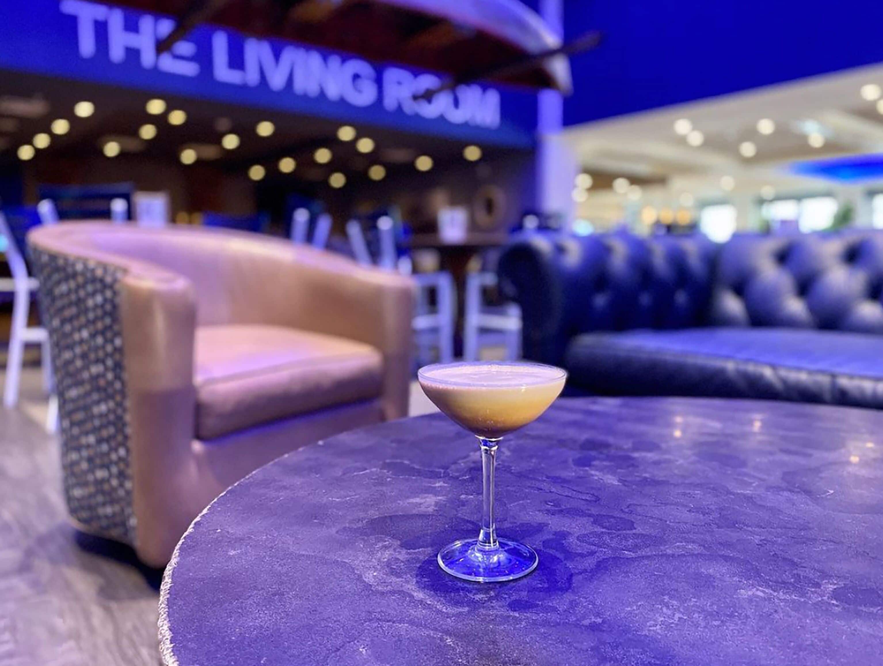 Een bar met een cocktail op een tafel, een bank en een bordje met de tekst 'THE LIVING ROOM'.