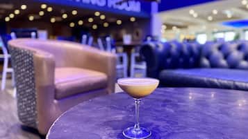 Een bar met een cocktail op een tafel, een bank en een bordje met de tekst 'THE LIVING ROOM'.