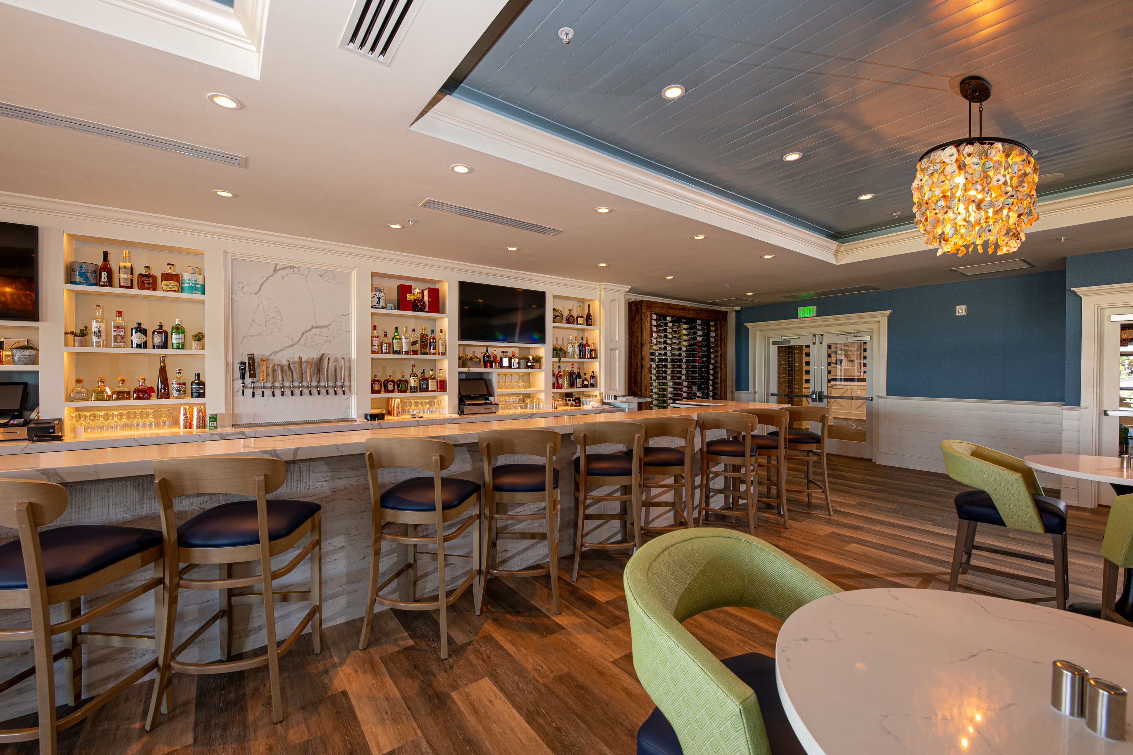 A bar area with wooden bar stools, a marble countertop, and shelves stocked with bottles.