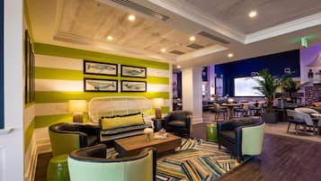 A modern lobby with striped green and white walls, a seating area with sofas and chairs, a large screen, and a plant.