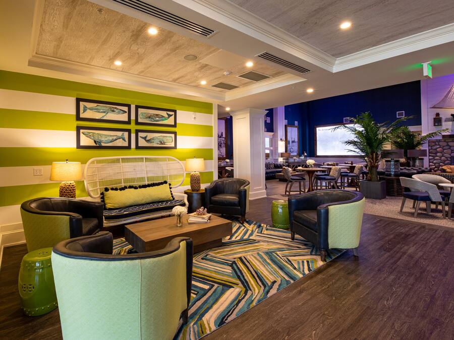 A modern lobby with striped green and white walls, a seating area with sofas and chairs, a large screen, and a plant.