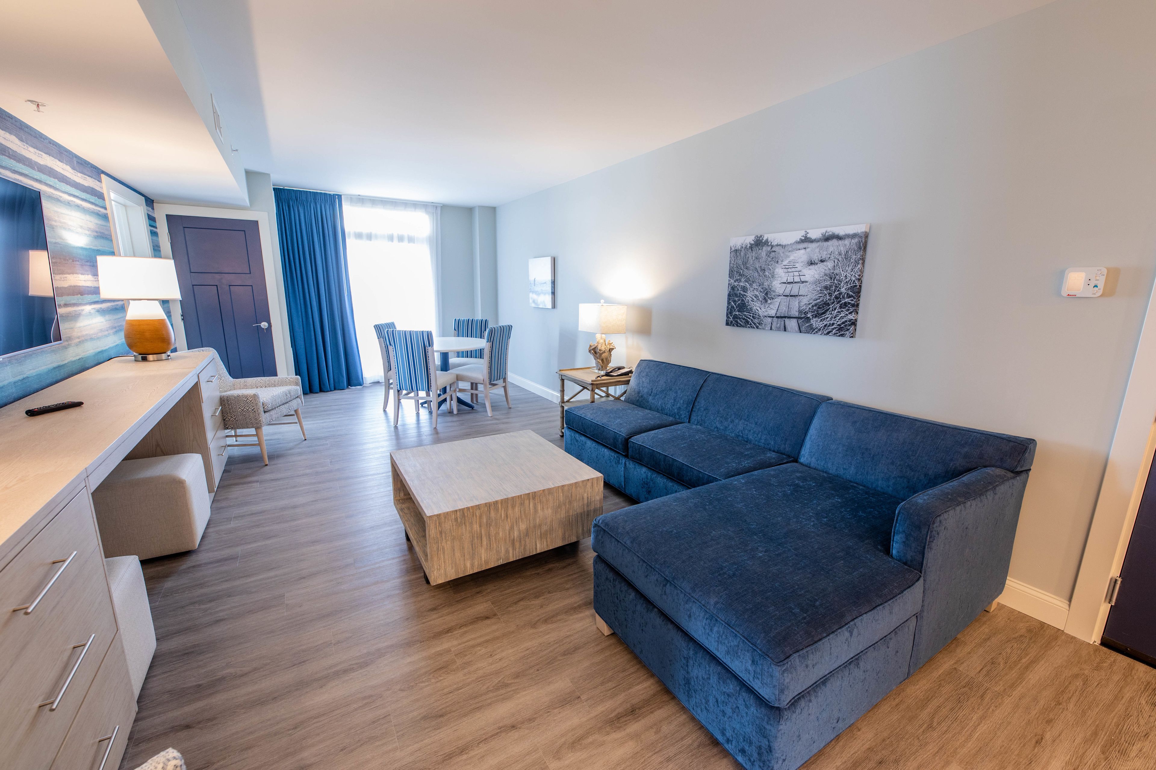 Uma sala de estar moderna com um sofá azul, mesa de centro de madeira e cadeiras listradas.