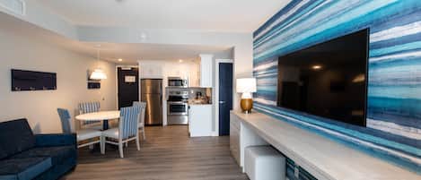 A modern kitchen with white cabinets, stainless steel appliances, and a large flat-screen TV mounted on the wall.