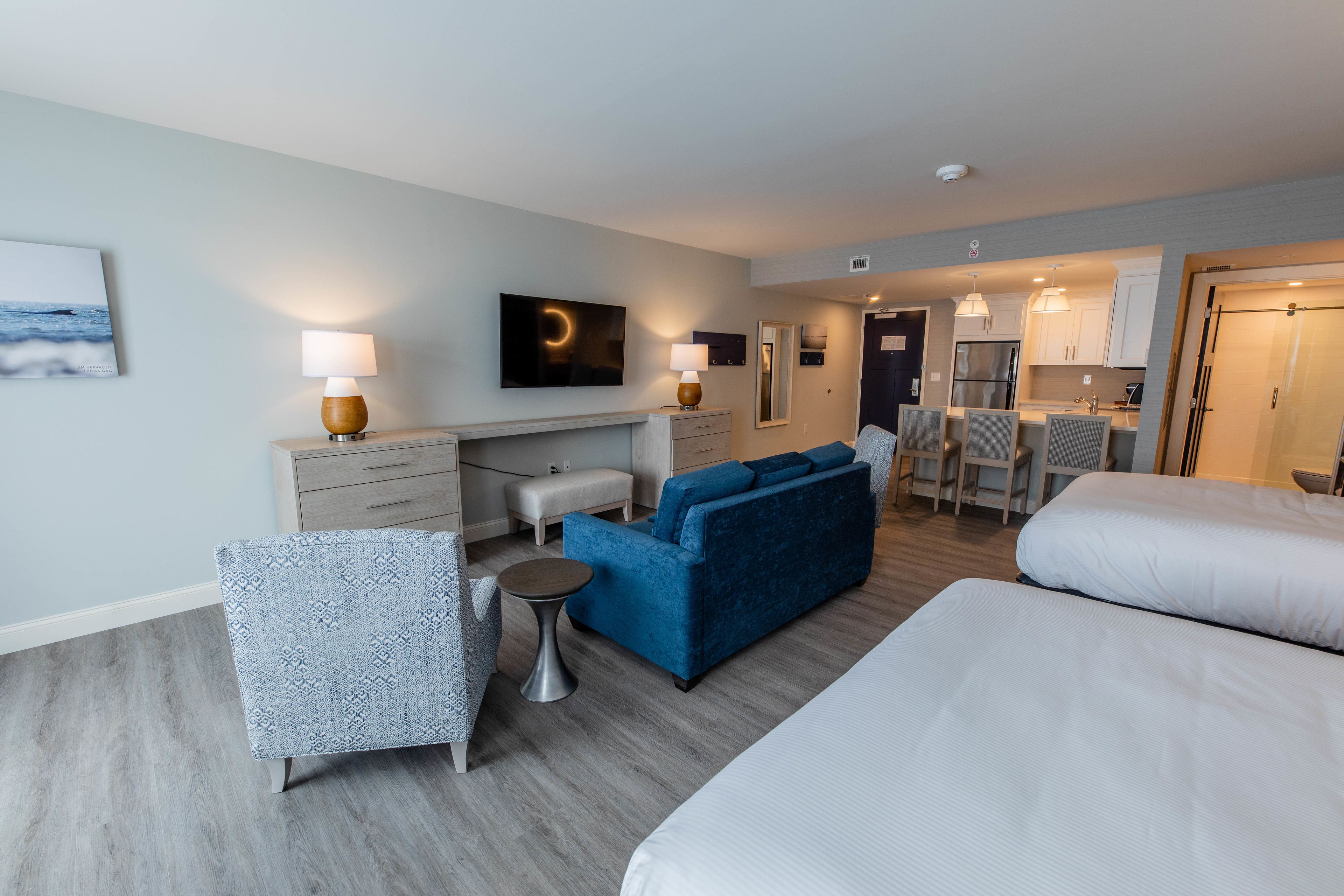 Habitación de hotel con sofá, una mesita, una silla, cama, televisor, zona de cocina y baño.