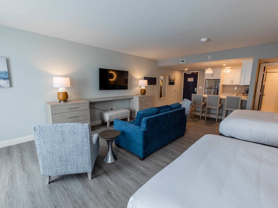 Habitación de hotel con sofá, una mesita, una silla, cama, televisor, zona de cocina y baño.