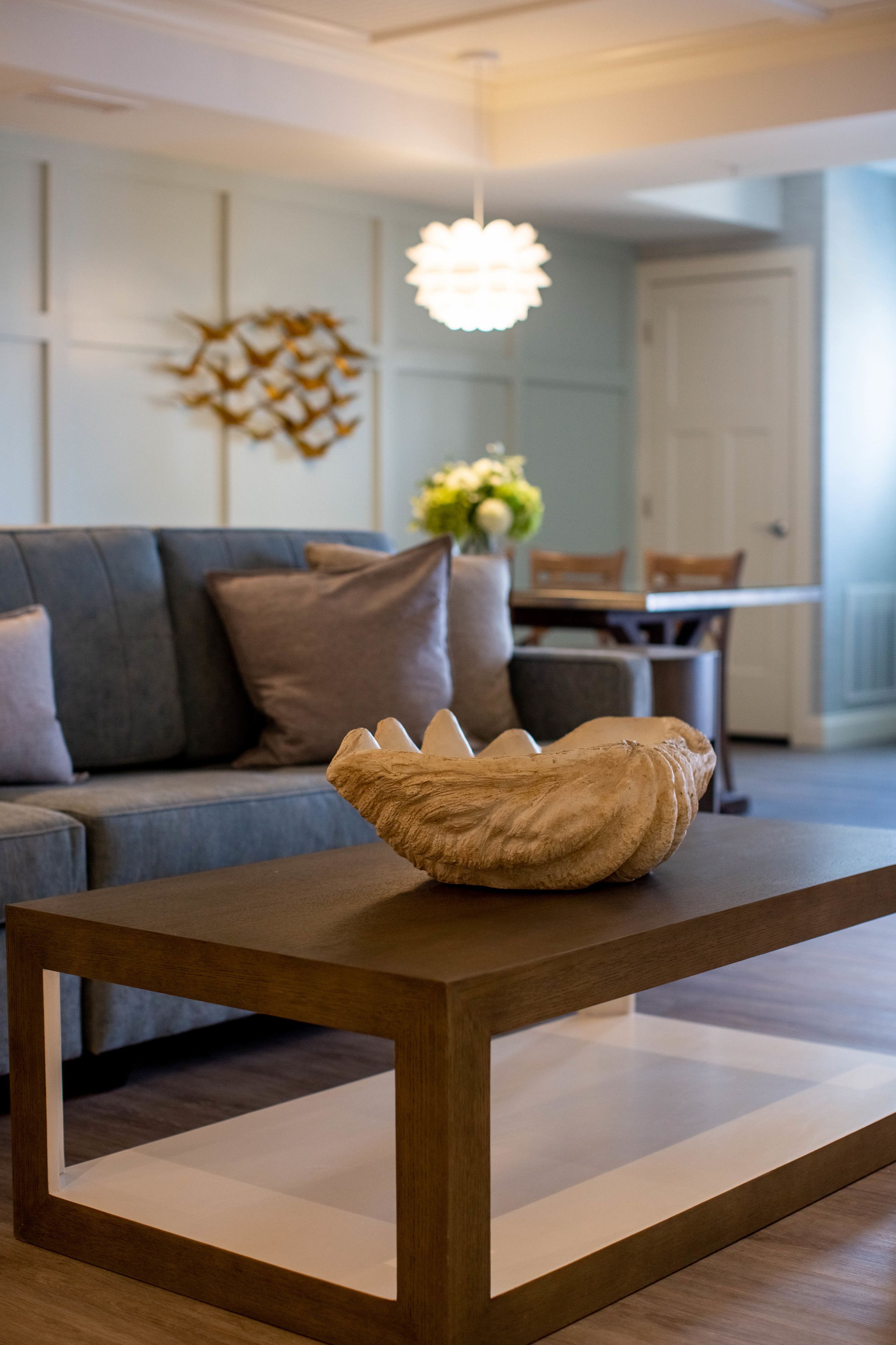 Un salón moderno con una mesa de centro de madera, un sofá gris y un elemento decorativo en la pared.