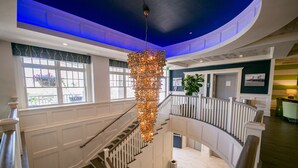 A multi-level interior with a central staircase, white paneling, and a hanging chandelier. - Hotel LBI (Beach Haven)