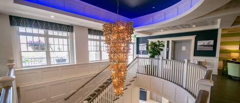 A multi-level interior with a central staircase, white paneling, and a hanging chandelier.