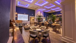 A spacious lounge area with a large screen displaying a welcome message, comfortable seating arrangements, and a decorative sailboat model. - Hotel LBI (Beach Haven)