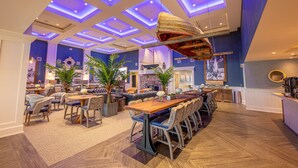 A spacious hotel lobby with a long wooden reception desk, multiple seating areas, and a ceiling with blue lighting. - Hotel LBI (Beach Haven)